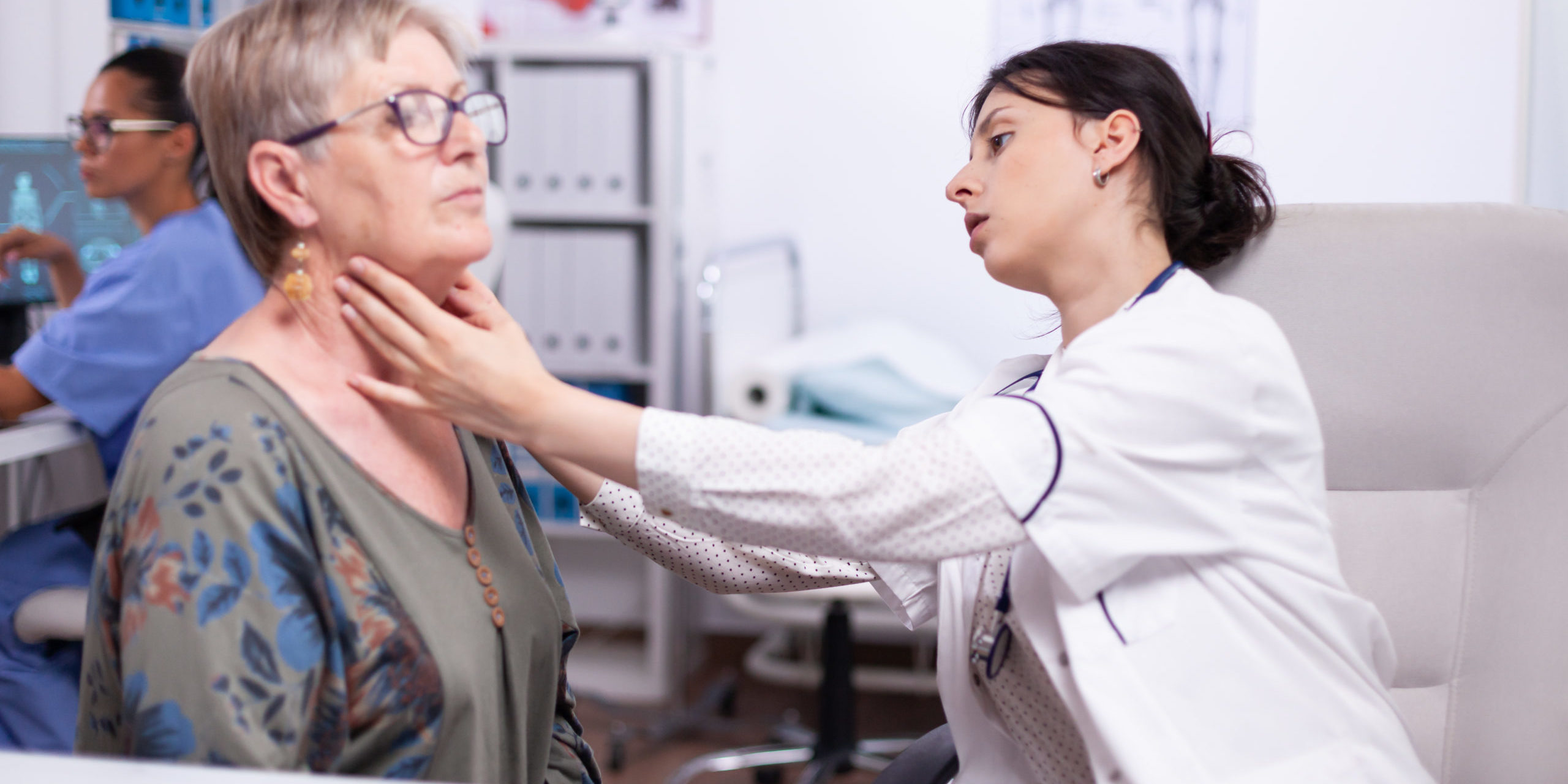 Young medic palpating neck of senior woman